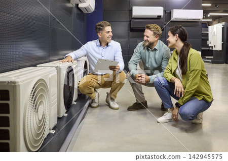 Salesman consults couple selecting air conditioners in modern appliance showroom Salesman consults couple selecting air conditioners in modern appliance showroom 142945575