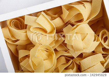 raw pappardelle pasta, pasta nests, in a paper box, top view, no people, raw pappardelle pasta, pasta nests, in a paper box, top view, no people, 142945829