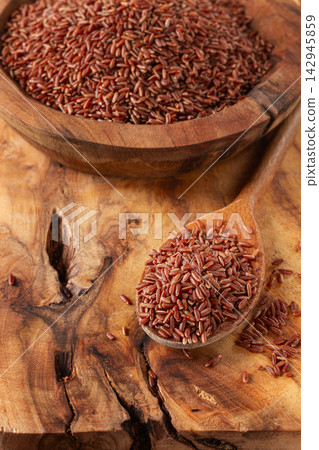 Natural red rice, in a wooden bowl and spoon on a wooden surface in rustic style, top view Natural red rice, in a wooden bowl and spoon on a wooden surface in rustic style, top view 142945859