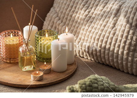 Group of lit candles and diffuser sticks arranged on a wooden tray with textured pillows Group of lit candles and diffuser sticks arranged on a wooden tray with textured pillows 142945979