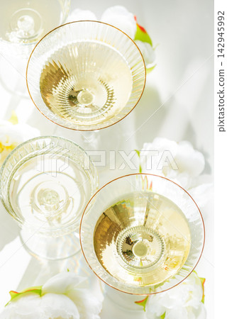 Four glasses filled with bubbly champagne and white flowers on a white background Four glasses filled with bubbly champagne and white flowers on a white background 142945992
