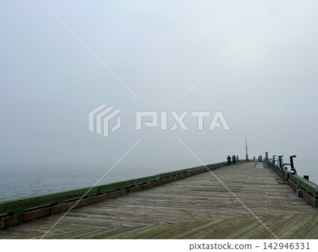 Long Wooden Fishing Pier Extending into Dense Coastal Fog 142946331