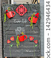 Decorative wooden wall featuring red teacup flower pots with hanging plants, red flowers, and text Enjoy Life. 142946434