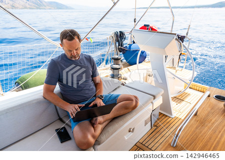 Focused man working on laptop aboard a sailing yacht. Productive remote office in a unique travel environment. Focused man working on laptop aboard a sailing yacht. Productive remote office in a unique travel environment. 142946465