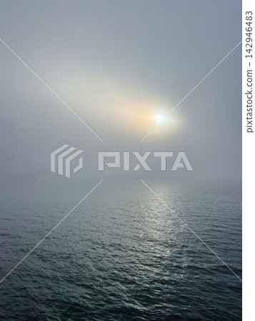 Glowing sun breaking through thick overcast fog over calm ocean water, creating a atmospheric moody seascape. Glowing sun breaking through thick overcast fog over calm ocean water, creating a atmospheric moody seascape. 142946483