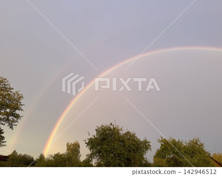 Brilliant double rainbow arching over green trees in rural landscape 142946512
