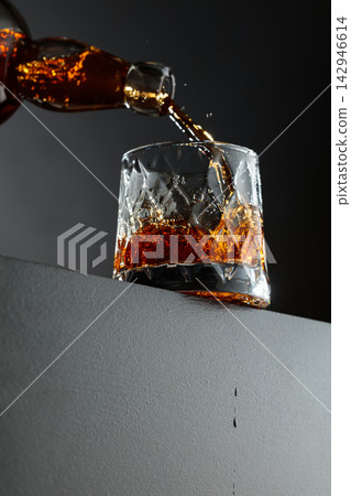 Whisky is poured from a bottle into a crystal glass. Whisky is poured from a bottle into a crystal glass. 142946614