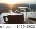 Close-Up of Coffee Cup and Water Glass Backlit by a Warm Sunset 142946922