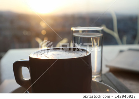 Close-Up of Coffee Cup and Water Glass Backlit by a Warm Sunset Close-Up of Coffee Cup and Water Glass Backlit by a Warm Sunset 142946922