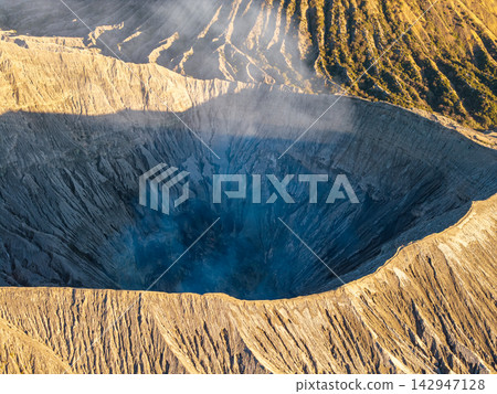 Deep volcanic crater glows with swirling blue smoke Deep volcanic crater glows with swirling blue smoke 142947128