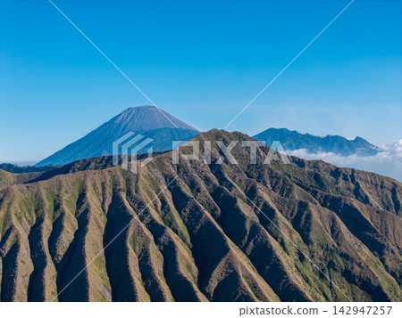 Rugged mountain ridges stretch beneath a clear blue sky Rugged mountain ridges stretch beneath a clear blue sky 142947257