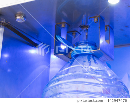 Automatic water dispenser filling a large plastic bottle with fresh liquid. Vending machine station with blue LED light. Close up of purification process 142947476
