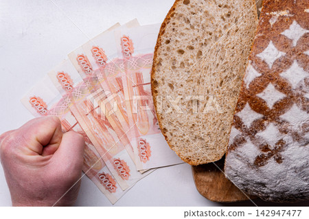 Clenched fist next to 5000 Russian Ruble banknotes and sliced bread. Concept of inflation and rising food prices Clenched fist next to 5000 Russian Ruble banknotes and sliced bread. Concept of inflation and rising food prices 142947477