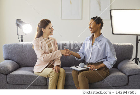 Diverse women shaking hands, smiling holding microphone for interview or media production Diverse women shaking hands, smiling holding microphone for interview or media production 142947603