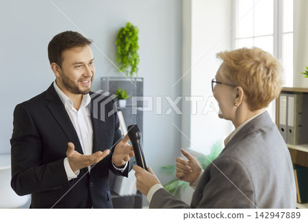 Reporter handing microphone to business speaker during interview in modern office Reporter handing microphone to business speaker during interview in modern office 142947889