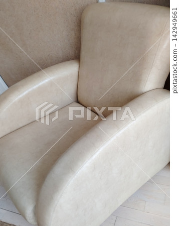 Modern beige leather armchair with curved arms and plush upholstery in minimalistic interior setting 142949661