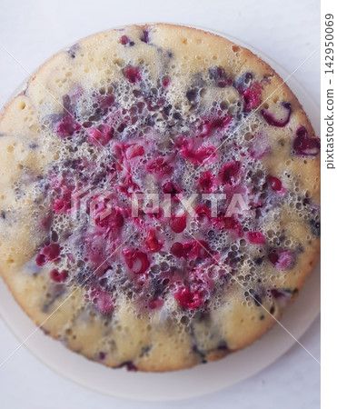 Round cake topped with red berries and bubbles on a white plate, overhead view 142950069