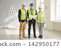 Confident engineers and contractors review blueprints in safety gear indoors 142950177
