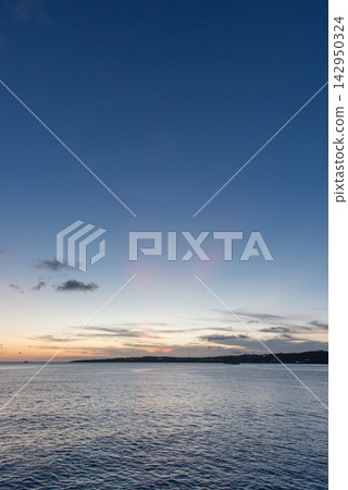 A calm sea with faint red crepuscular rays visible at dusk. A calm sea with faint red crepuscular rays visible at dusk. 142950324
