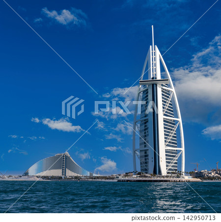 Iconic Burj Al Arab and Jumeirah Beach Hotel on Dubai coastline under blue sky Iconic Burj Al Arab and Jumeirah Beach Hotel on Dubai coastline under blue sky 142950713