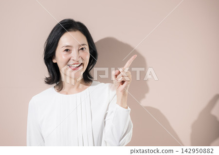 A Japanese middle-aged woman smiles and points; a woman in her 50s introduces recommendations, new discoveries, products, and services. A Japanese middle-aged woman smiles and points; a woman in her 50s introduces recommendations, new discoveries, products, and services. 142950882