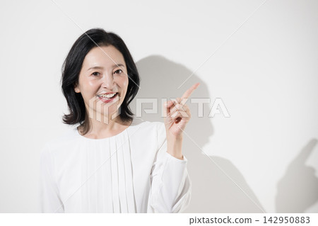 [White background] A smiling middle-aged Japanese woman points, suggesting products or services such as recommendations, new discoveries, hints, or choices. 142950883