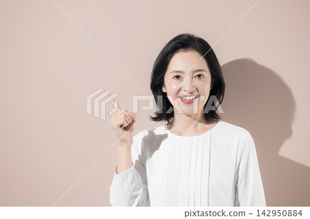 A Japanese middle-aged woman smiles and points; a woman in her 50s introduces recommendations, new discoveries, products, and services. A Japanese middle-aged woman smiles and points; a woman in her 50s introduces recommendations, new discoveries, products, and services. 142950884