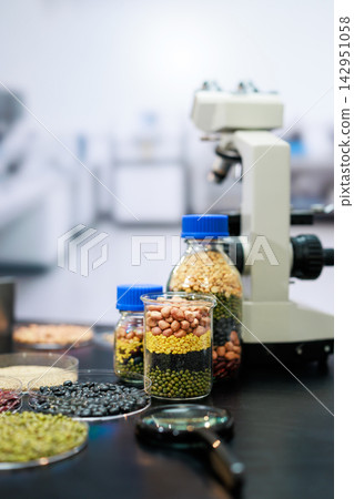 Jars of colorful beans, grains and seeds beside a microscope in a laboratory, food research, nutrition testing and agricultural quality control. Jars of colorful beans, grains and seeds beside a microscope in a laboratory, food research, nutrition testing and agricultural quality control. 142951058