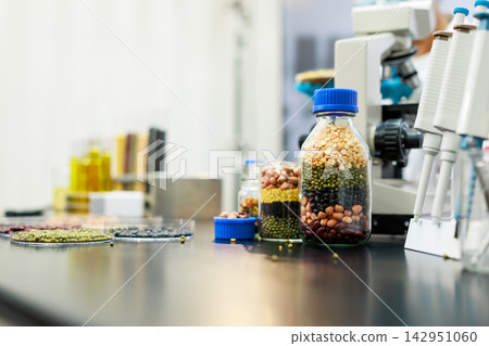 Glass jars filled with colorful beans and grains beside laboratory equipment on a clean workbench, food testing, nutrition research and quality control. Glass jars filled with colorful beans and grains beside laboratory equipment on a clean workbench, food testing, nutrition research and quality control. 142951060