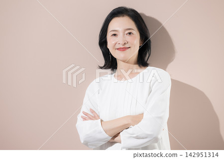 [粉紅色背景] 一位面帶微笑的日本中年女性，雙臂交叉抱在胸前，是一位自信可靠的50多歲女性領導者或專業人士。 142951314