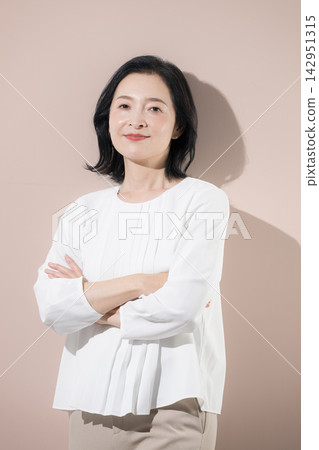 [粉紅色背景] 一位面帶微笑的日本中年女性，雙臂交叉抱在胸前，是一位自信可靠的50多歲女性領導者或專業人士。 142951315