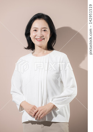 [粉紅背景] 一位面帶微笑、面向前方的日本中年女性的肖像，她是一位健康、值得信賴、令人安心的五十多歲女性。 142951519