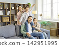 Smiling mother and father with daughters playing on sofa in bright home interior 142951995