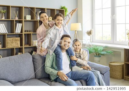 Smiling mother and father with daughters playing on sofa in bright home interior Smiling mother and father with daughters playing on sofa in bright home interior 142951995