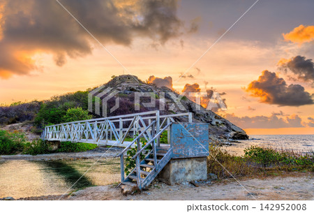 Scenic view of a Lagoon footbridge leading toward Fort Barrington on a coastal hill in Antigua and Barbuda at dramatic sunset. Scenic view of a Lagoon footbridge leading toward Fort Barrington on a coastal hill in Antigua and Barbuda at dramatic sunset. 142952008