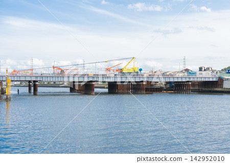 A large crane with its boom lowered at a construction site for replacing a bridge over a river. A large crane with its boom lowered at a construction site for replacing a bridge over a river. 142952010