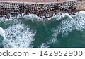 Aerial view of dramatic waves hitting concrete breakwater along a scenic coastal promenade, showcasing nature's power and human engineering. ocean, travel, and coastal infrastructure themes. 142952900