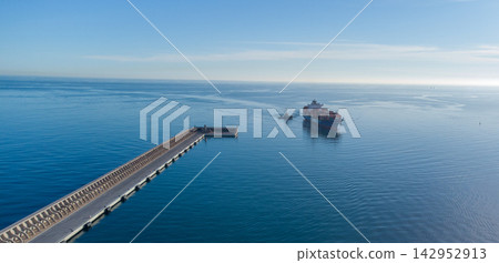 Majestic cargo ship sails under clear skies, nearing a coastal pier against a tranquil sea backdrop. ideal for illustrating global trade, maritime industry, or serene ocean travel concepts. Majestic cargo ship sails under clear skies, nearing a coastal pier against a tranquil sea backdrop. ideal for illustrating global trade, maritime industry, or serene ocean travel concepts. 142952913
