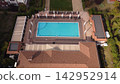 Aerial view of a luxurious outdoor swimming pool oasis with white umbrellas, lounge chairs, and lush greenery, ideal for vacation and resort concepts. 142952914