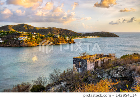 Scenic landscape view of the historic Fort Barrington ruins overlooking a tropical bay and coastal hills at sunset in Antigua and Barbuda. Scenic landscape view of the historic Fort Barrington ruins overlooking a tropical bay and coastal hills at sunset in Antigua and Barbuda. 142954114
