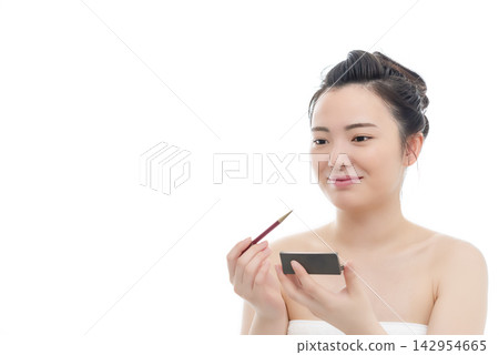 一位年輕女子在白色背景前化眼妝。 142954665