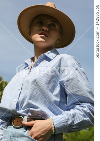 Woman stands in a blue shirt and hat looking up outdoors 142955359