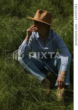 Model sits in green grass while wearing a hat and thinking Model sits in green grass while wearing a hat and thinking 142955361
