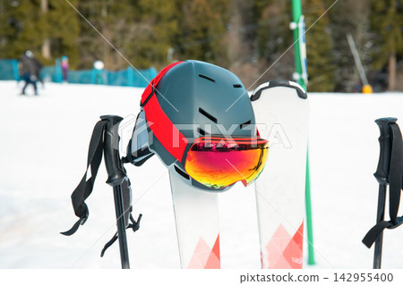 Ski helmet and colorful goggles are positioned on ski poles in snow Ski helmet and colorful goggles are positioned on ski poles in snow 142955400