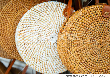 Rattan bags. Round rattan bags hang from hooks in a vibrant artisan market Rattan bags. Round rattan bags hang from hooks in a vibrant artisan market 142955420
