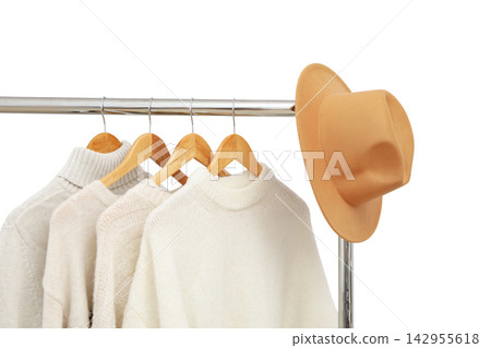 Fall clothing. Cozy sweaters hang on rack alongside a fashionable hat, PNG Fall clothing. Cozy sweaters hang on rack alongside a fashionable hat, PNG 142955618