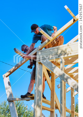 Installation of rafter system of timber frame house, workers fastening rafter leg while holding it together. 142957687