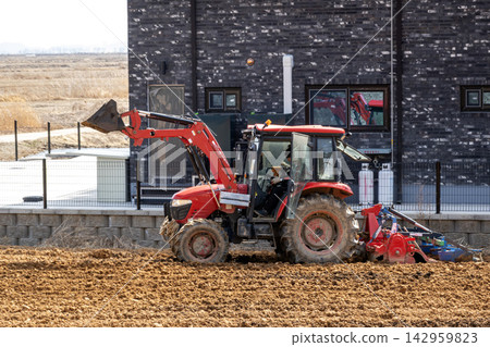 A red tractor plowing and preparing the field. A red tractor plowing and preparing the field. 142959823
