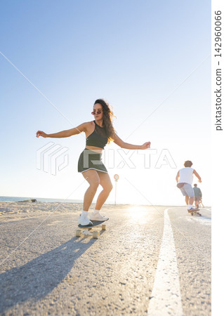 Skater enjoys sunny day on boardwalk by the beach while others ride in background Skater enjoys sunny day on boardwalk by the beach while others ride in background 142960066