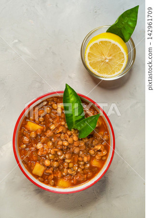 Top view of healthy lentil soup or stew in bowl served with fresh lemon slice on grey concrete background. Top view of healthy lentil soup or stew in bowl served with fresh lemon slice on grey concrete background. 142961709